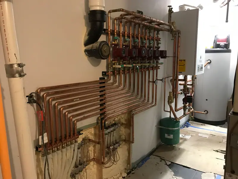 Bank of seven red circulator pumps on polished copper piping beside a hot water storage tank.