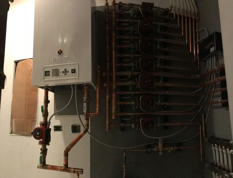 Wall-hung ACV Prestige boiler connected to a vertical row of circulator pumps by copper piping.