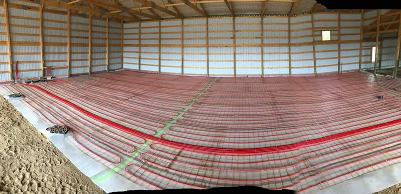 Red PEX radiant tubing laid over wire mesh across a large pole-barn floor before the concrete pour.