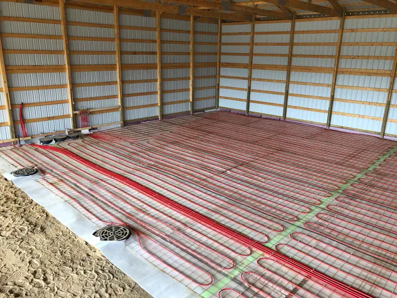 Radiant PEX tubing secured to wire mesh across a pole-barn slab with floor drains set in place.