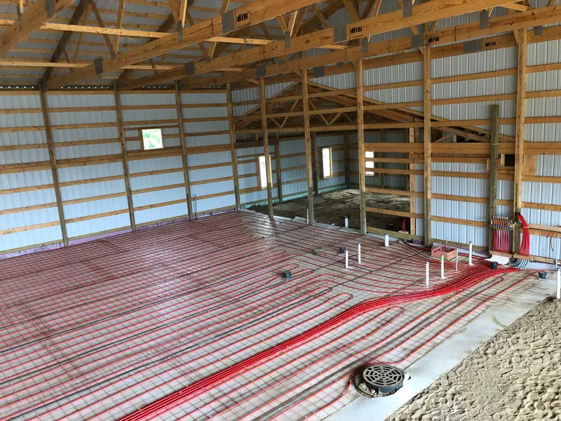 Radiant tubing and a wall manifold installed across a large residential slab under construction.