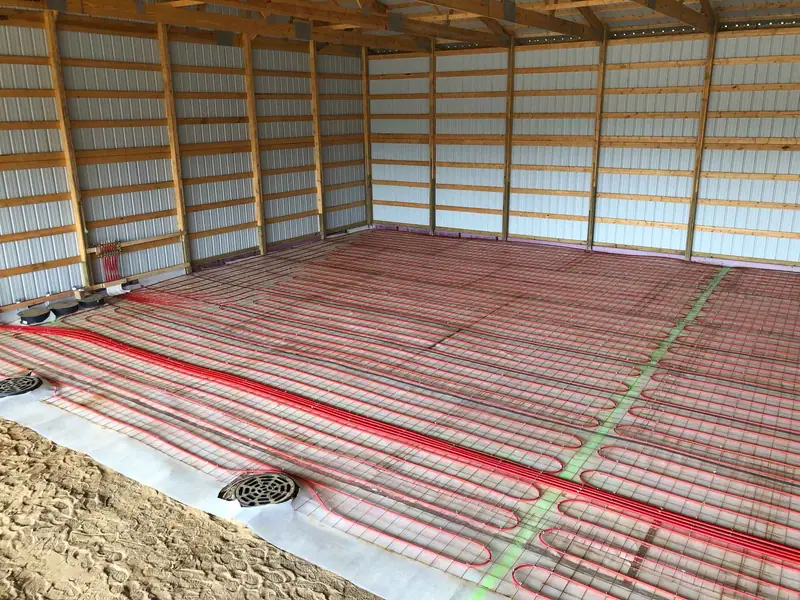 Wide view of red radiant tubing installed across a pole-barn floor before concrete is poured.