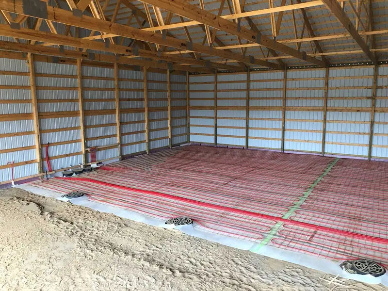 Radiant floor loops feeding into a wall manifold inside a steel-framed pole barn.
