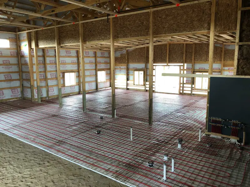 Radiant floor tubing routed around support posts and connected to a wall manifold.