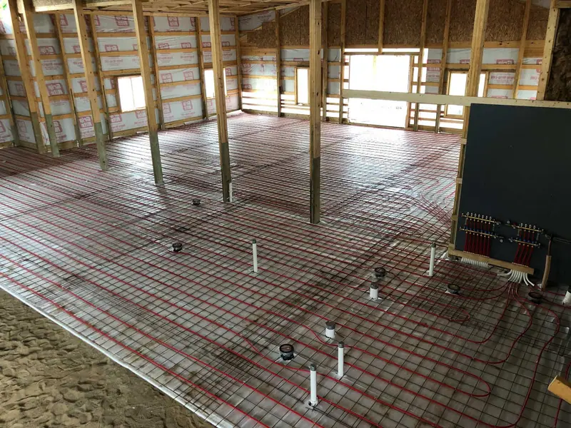 Dense grid of radiant PEX tubing over rebar with manifolds set for a concrete floor pour.