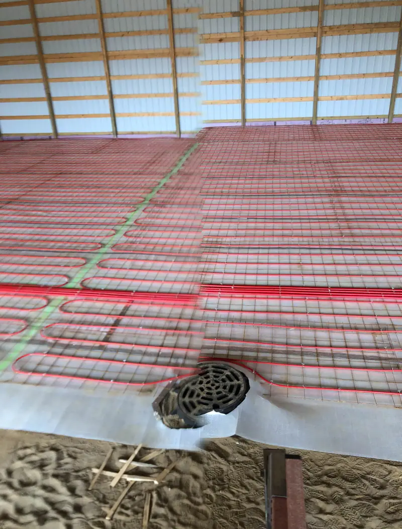 Close view of radiant PEX loops and a floor drain over a sand base before the pour.