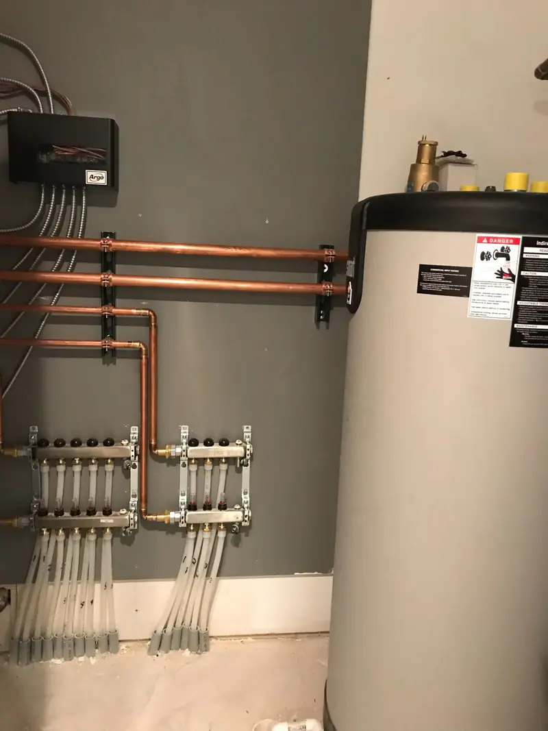 Stainless steel PEX radiant floor manifolds with flow meters beside an indirect hot water tank.