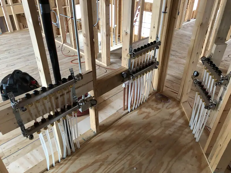 Three PEX distribution manifolds feeding radiant floor loops during a home’s framing stage.