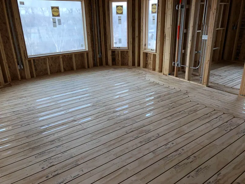 Grooved radiant subfloor panels with embedded PEX tubing across a sunlit room.